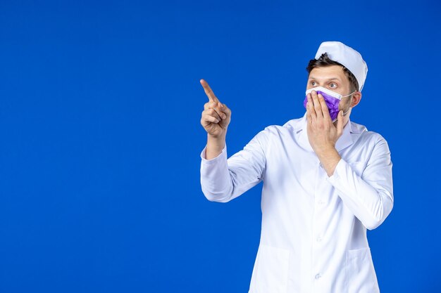 Front view of male doctor in medical suit and purple mask on blue 