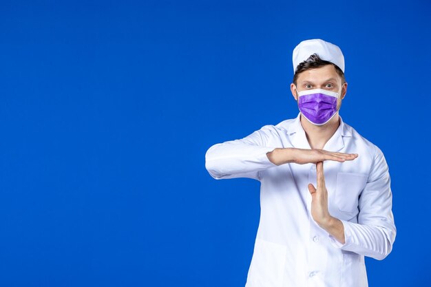 Vista frontale del medico maschio in tuta medica e maschera viola sull'azzurro