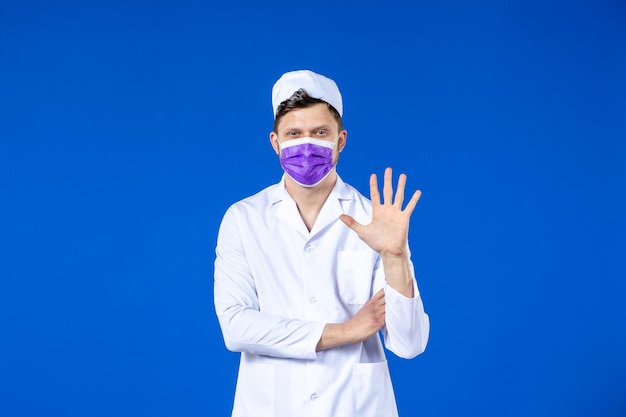 Вид спереди мужского врача в медицинском костюме и фиолетовой маске на синем