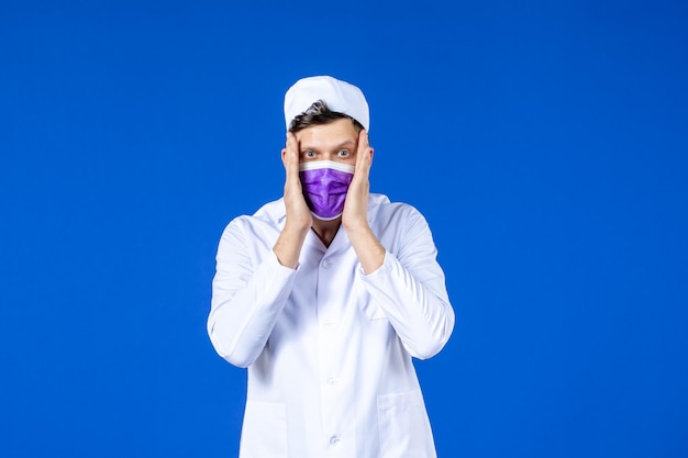 Foto gratuita vista frontale del medico maschio in tuta medica e maschera viola sull'azzurro