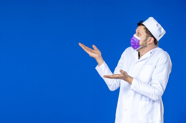 Front view of male doctor in medical suit and purple mask on blue 