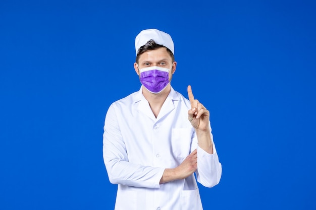 Front view of male doctor in medical suit and purple mask counting on blue