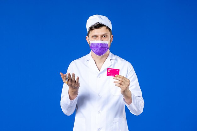 医療スーツと青の注射とクレジットカードを保持している紫色のマスクの男性医師の正面図