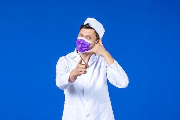 Vista frontale del medico maschio in tuta medica e maschera viola che imita la telefonata sull'azzurro