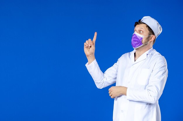 Front view of male doctor in medical suit and purple mask talking to someone aside on blue 