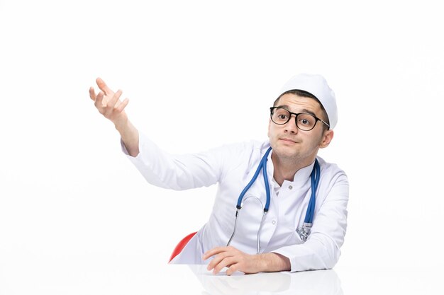 Front view male doctor in medical suit sitting behind desk