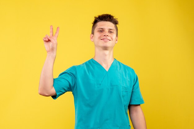 Front view of male doctor in medical suit smiling on yellow wall