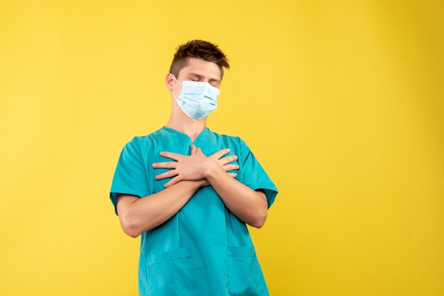 Front view of male doctor in medical suit and sterile mask on a yellow wall