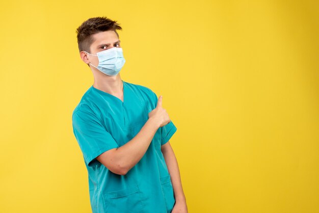 医療スーツと黄色の壁に滅菌マスクの男性医師の正面図