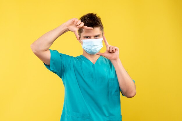 Front view of male doctor in medical suit and sterile mask on yellow wall