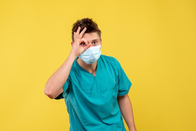 医療スーツと黄色の壁に滅菌マスクの男性医師の正面図