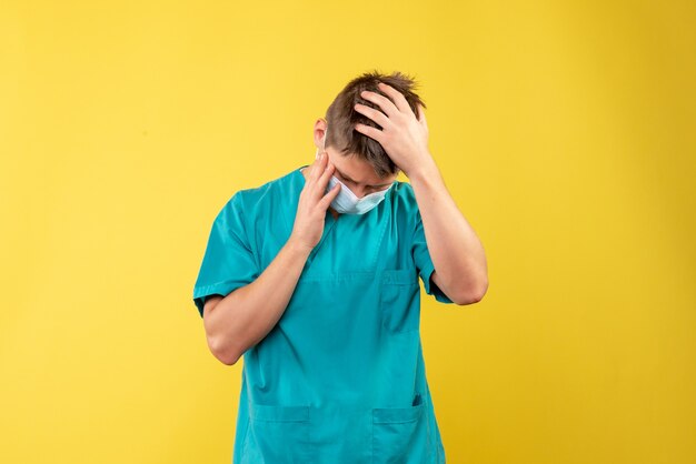 Front view of male doctor in medical suit and sterile mask on yellow wall