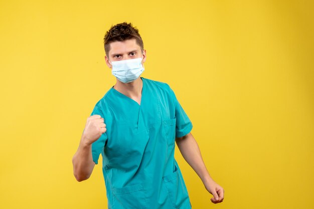 Front view of male doctor in medical suit and sterile mask on yellow wall