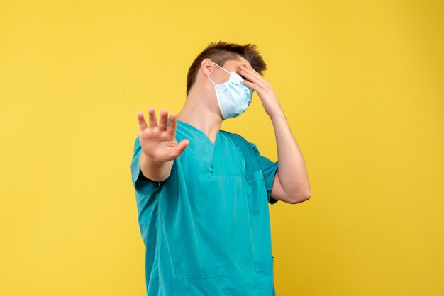 Front view of male doctor in medical suit and sterile mask on yellow wall