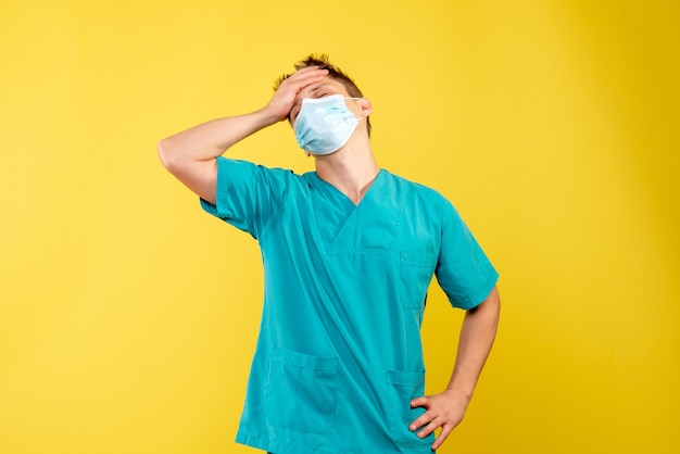 Front view of male doctor in medical suit and sterile mask on yellow wall