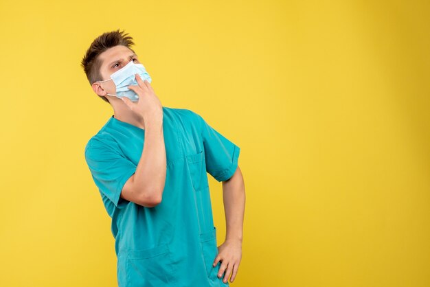 Front view of male doctor in medical suit and sterile mask on yellow wall