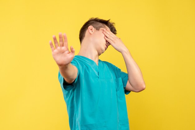 Front view of male doctor in medical suit stressed on yellow wall