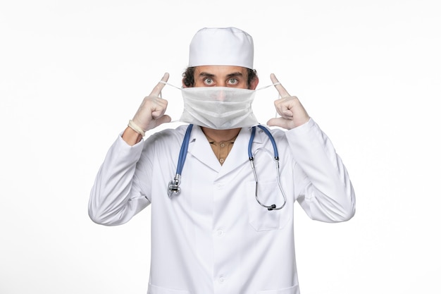白い壁のコロナウイルスウイルスパンデミック医学のコロナウイルスに対して彼のマスクを身に着けている医療スーツの正面図男性医師