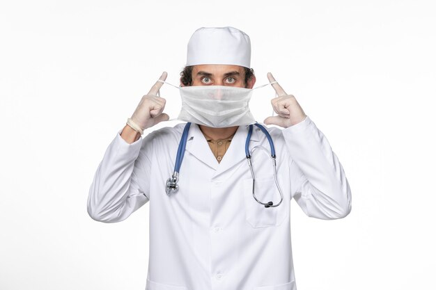 Front view male doctor in medical suit wearing his mask against coronavirus on white wall coronavirus virus pandemic medicine