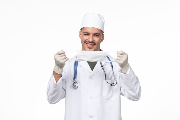 医療スーツを着て、白い机の上のコロナウイルスに対するマスクを身に着けている正面図の男性医師ウイルス感染症のパンデミック
