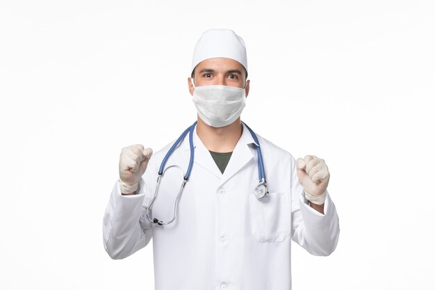 Вид спереди мужчина-врач в медицинском костюме и в маске против ликования covid на белой стене лекарство от пандемического вируса covid