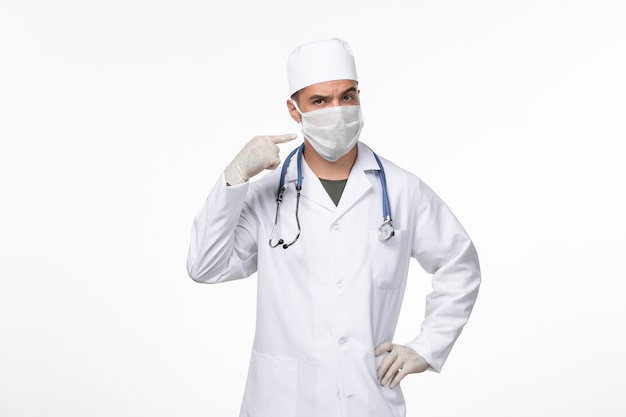 Вид спереди мужчина-врач в медицинском костюме и в маске против всплеска covid на белой стене пандемия вируса covid- болезни
