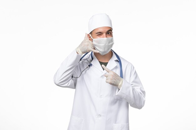 Front view male doctor in medical suit and wearing a mask against covid on the white desk covid disease medicine pandemic virus