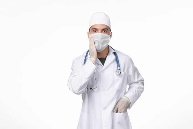 医療スーツを着た正面図の男性医師と白い机の上のcovidに対してマスクを身に着けているcovid医学パンデミック