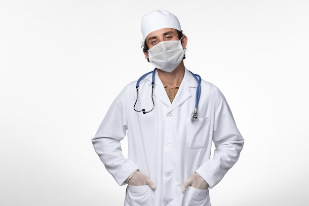 의료 복을 입은 남성 의사와 마스크를 착용 한 남성 의사는 흰 벽에 감염된 코로나 바이러스에 대한 보호막입니다.