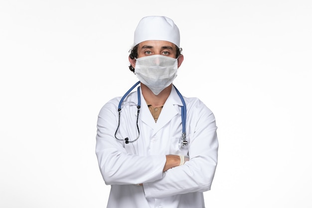 Front view male doctor in medical suit wearing mask as a protection from covid- on white desk virus illness health covid- pandemic