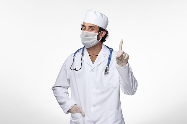 医療スーツを着て、白い壁の病気ウイルスのcovidパンデミックからの保護としてマスクを身に着けている正面図の男性医師