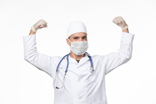 흰 벽에 covid- flexing으로 인해 의료 복을 입은 남성 의사와 마스크 착용 전면보기 covid- 바이러스 의학 유행병