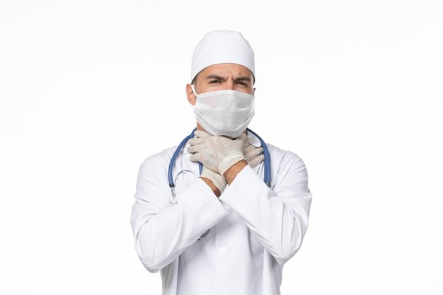 Front view male doctor in medical suit and wearing mask due to covid- on white desk covid- pandemic virus disease