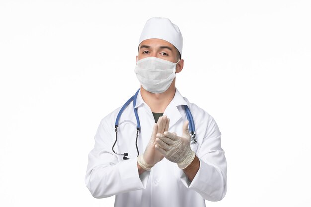 医療スーツを着て、白い机の病気ウイルスのパンデミック病のためにマスクを着用している正面図の男性医師