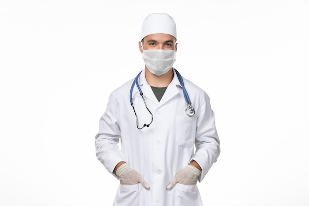 白い壁の病気のcovid-pandemicウイルス病のために医療スーツとマスクを身に着けている正面図の男性医師