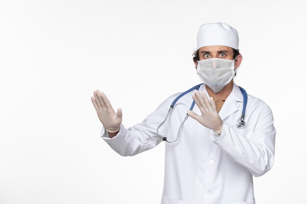 ライトホワイトウォールウイルスコロナウイルスパンデミック病からの保護として滅菌マスクを着用した医療スーツの正面図男性医師