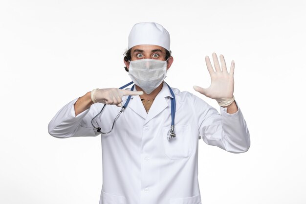 Front view male doctor in medical suit wearing sterile mask as a protection from covid- on white desk virus illness covid- pandemic