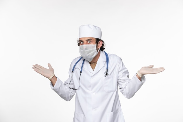 白い床のウイルスコロナウイルスパンデミック病のcovidからの保護として滅菌マスクを身に着けている医療スーツの正面図男性医師