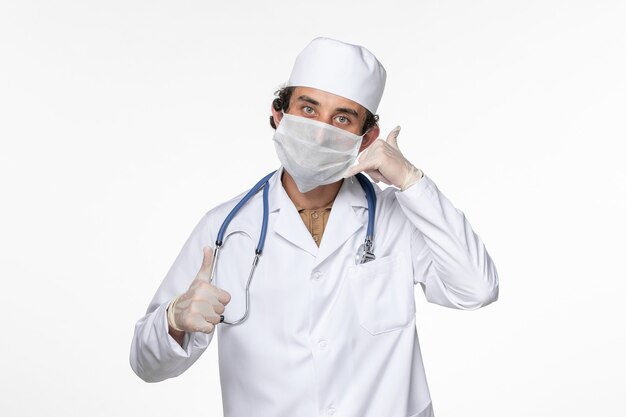 Front view male doctor in medical suit wearing sterile mask as a protection from covid on the white wall virus coronavirus pandemic disease