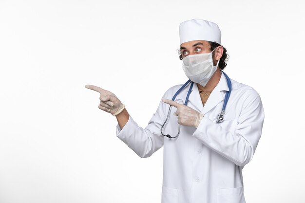 Front view male doctor in medical suit wearing sterile mask as a protection from covid- on white wall virus illness covid pandemic disease