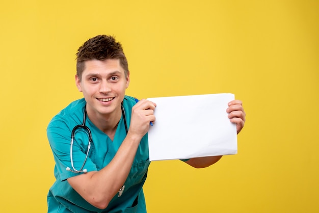 Front view of male doctor in medical suit with analysis smiling on yellow wall