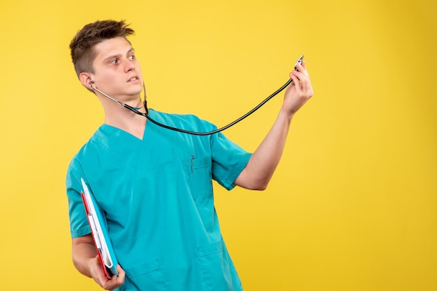 Front view of male doctor in medical suit with analysis and stethoscope on a yellow wall