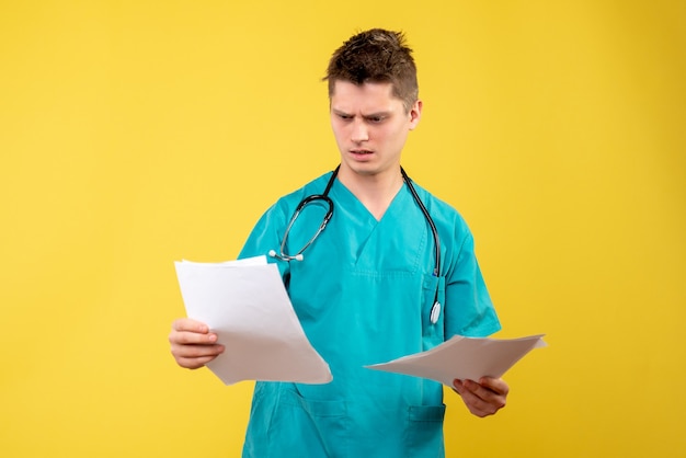 Front view of male doctor in medical suit with analysis on a yellow wall