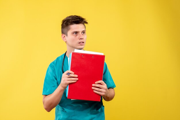 Front view of male doctor in medical suit with analysis on a yellow wall