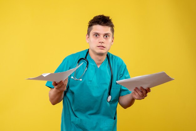Вид спереди мужского врача в медицинском костюме с анализом на желтой стене