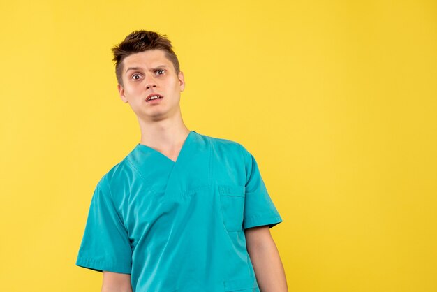 Front view of male doctor in medical suit with confused face on a yellow wall