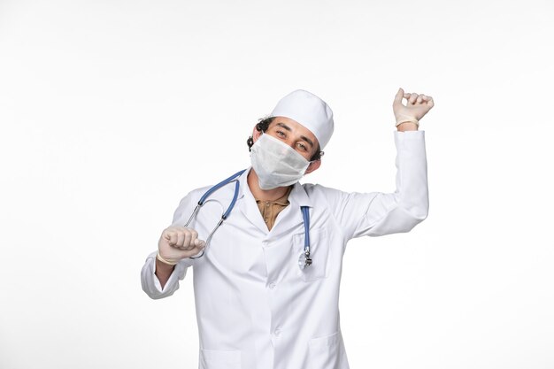 白い壁のスプラッシュウイルスコロナウイルスパンデミックでの共同ダンスからの保護としてマスク付きの医療スーツを着た正面図の男性医師