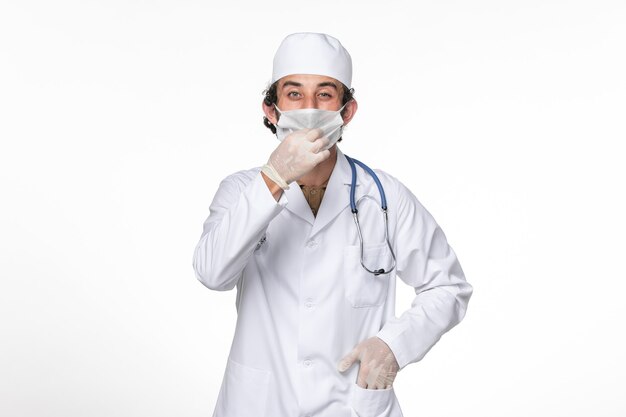 Front view male doctor in medical suit with mask as a protection from covid- on light-white wall coronavirus virus pandemic medicine