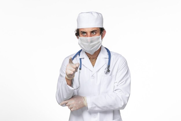 Front view male doctor in medical suit with mask as a protection from covid- on light white wall virus splash coronavirus pandemic