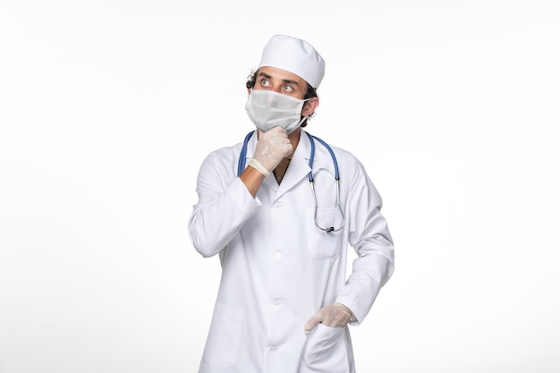 Front view male doctor in medical suit with mask as a protection from covid- thinking on white wall coronavirus virus pandemic medicine